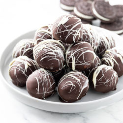 A white dessert stand with a stack of Oreo Truffles on top and Oreo Cookies in the background.