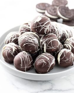 A white dessert stand with a stack of Oreo Truffles on top and Oreo Cookies in the background.