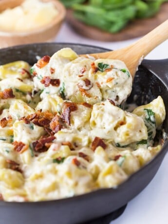 A spoon scooping out tortellini al forno from a black cast iron skillet.