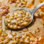 A close up view of a spoon filled with lentil soup with ham.