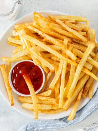 A white plate full of homemade McDonald's French Fries and kechup.