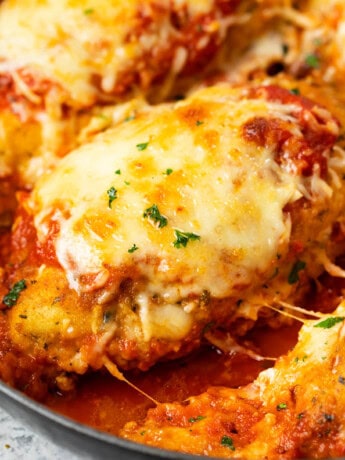 A breaded chicken breast topped with melted mozzarella in a pan with marinara sauce for Baked Chicken Parmesan.