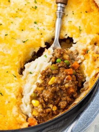 A large spoon scooping Shepherds Pie from a casserole dish.