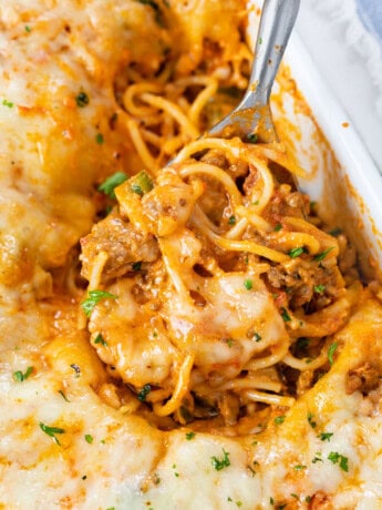 A casserole dish filled with Baked Spaghetti with a spoon scooping it up.