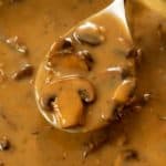 A spoon full of creamy mushroom gravy from a skillet.