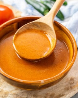 A bowl with a wooden spoon filled with homemade enchilada sauce.