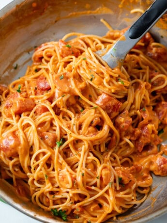 A skillet with creamy tomato pasta with kitchen tongs.