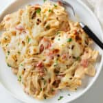 A white plate with cheesy Chicken Spaghetti with a fork on the side.
