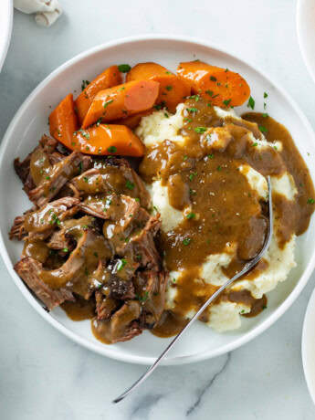 Mississippi Pot Roast on a white plate with carrots, mashed potatoes, and gravy.
