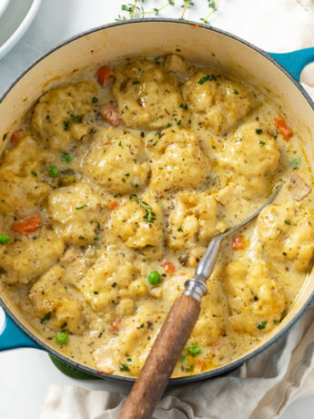 Chicken and Dumplings in a Dutch oven with a spoon on the side.