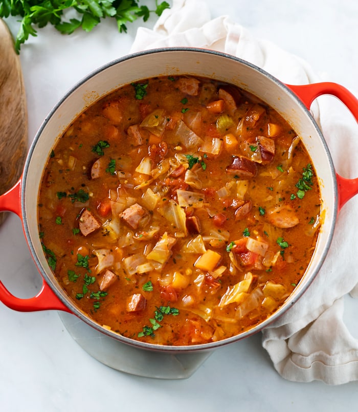 A red Dutch oven filled with Cabbage Soup with vegetables and Kielbasa.
