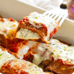 Eggplant Rollatini with ricotta filling being pulled up from a casserole dish by a spatula.