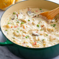Chicken a la King in a green Dutch oven with a wooden spoon.