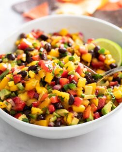 Mango Salsa in a white bowl with a spoon scooping it up.