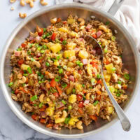 Pineapple Fried Rice in a stainless steel skillet with a silver spoon on the side.