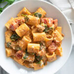Creamy Tomato Spinach Pasta in a white bowl with tomatoes, sausage, and spinach.