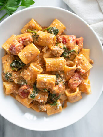 Tomato Spinach Pasta in a white bowl with parmesan cheese sprinkled on top.