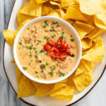 Rotel Dip in a white bowl on a platter with tortilla chips.