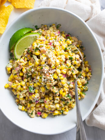 Mexican Street Corn Salad in a bowl with Cotija cheese on top and a spoon on the side.