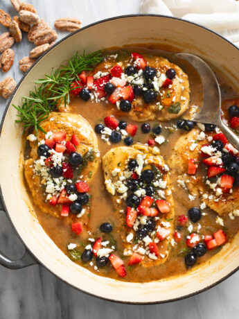 Balsamic Chicken in a skillet with feta and blueberries and strawberries on top an a spoon on the side.