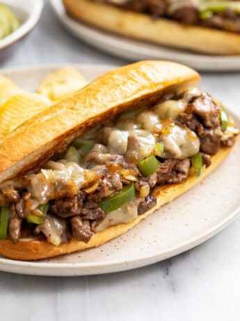 A Philly Cheesesteak Sandwich on a plate with potato chips in the back.