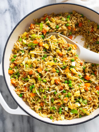 A white skillet with Vegetable Fried Rice and a white spoon on the side.