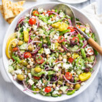 Greek Salad in a white bowl with vegetables, chickpeas, dressing, and feta.