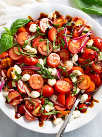 Tomato Salad in a white bowl with fresh basil, mozzarella, red onions, and balsamic glaze.