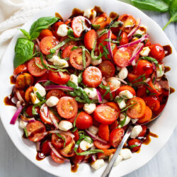 Tomato Salad in a white bowl with mozzarella pearls, fresh basil, red onions, and homemade balsamic dressing.