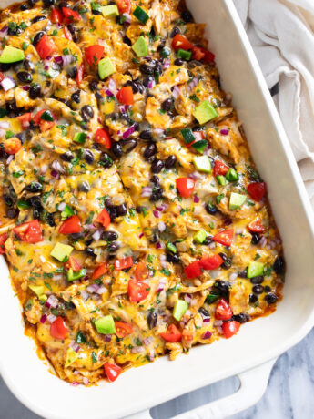 Chicken Enchilada Casserole in a white casserole dish with assorted colorful toppings on top.