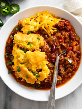Chili Corn Casserole in a white bowl with a spoon on the side and cheese on top.