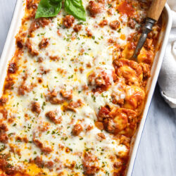 Ravioli Lasagna in a white casserole dish with fresh basil on top and a serving spoon on the side.