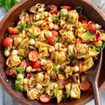 Caprese Pasta Salad in a wooden bowl with balsamic glaze drizzled on top with fresh basil.