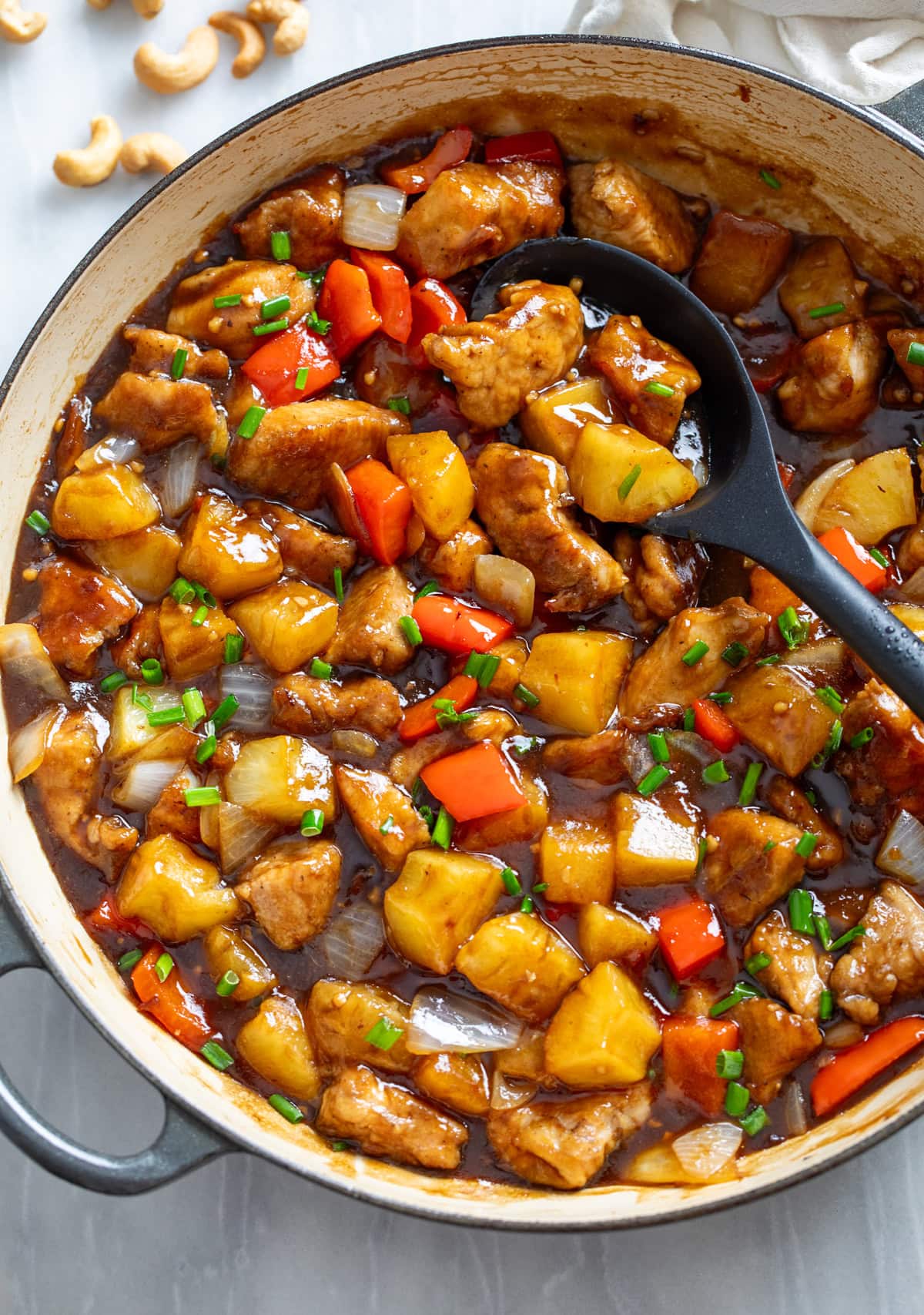 Pineapple Chicken in a skillet with pineapples, peppers, onions, and a glossy sauce.