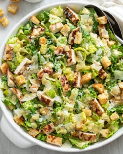 Chicken Caesar Salad in a white bowl with grilled chicken parmesan cheese, homemade dressing, and homemade croutons.