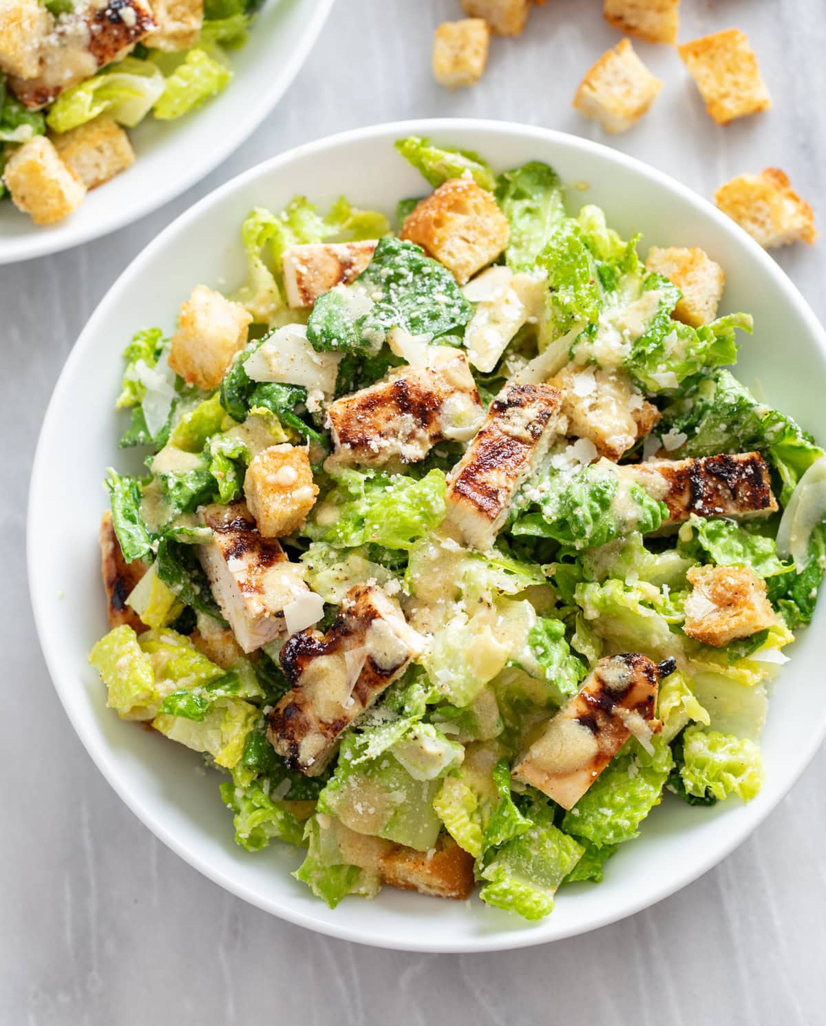Chicken Caesar Salad in a white bowl with grilled chicken homemade dressing and croutons, and parmesan cheese.