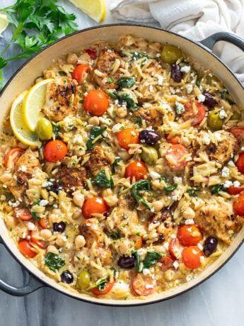 Greek Chicken Orzo in a skillet with sauce, orzo, chicken, chickpeas, spinach, tomatoes, olives, and feta.