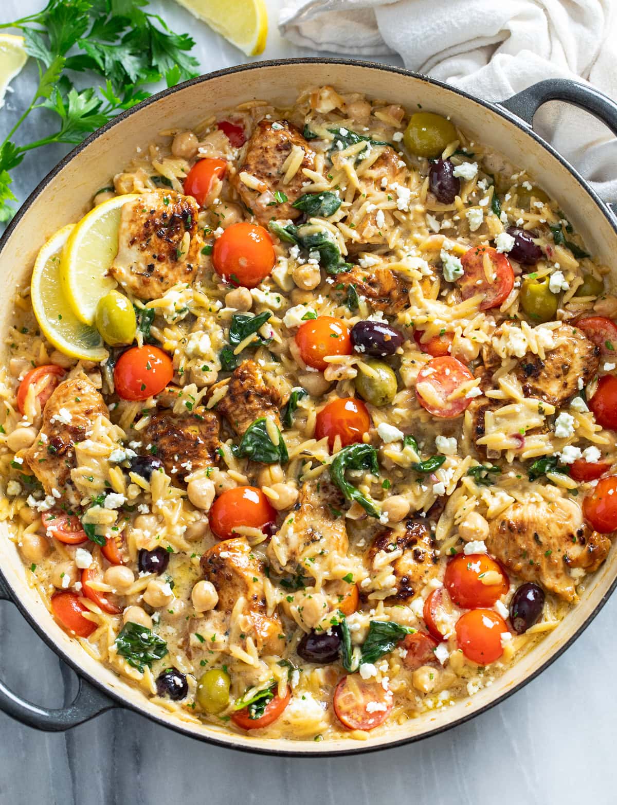 Greek Chicken Orzo in a skillet with sauce, orzo, chicken, chickpeas, spinach, tomatoes, olives, and feta.