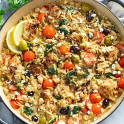 Greek Chicken Orzo in a skillet with olives, tomatoes, spinach, chickpeas, chicken and feta.