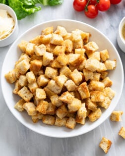 Homemade Croutons in a white bowl on a white marble surface.