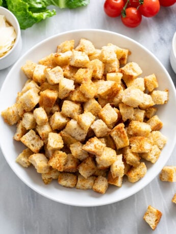 Homemade Croutons in a white bowl on a white marble surface.