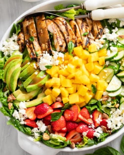 Mango Salad in a white bowl with grilled chicken, avocado, strawberry, and cucumber with mangos, feta, and dressing.