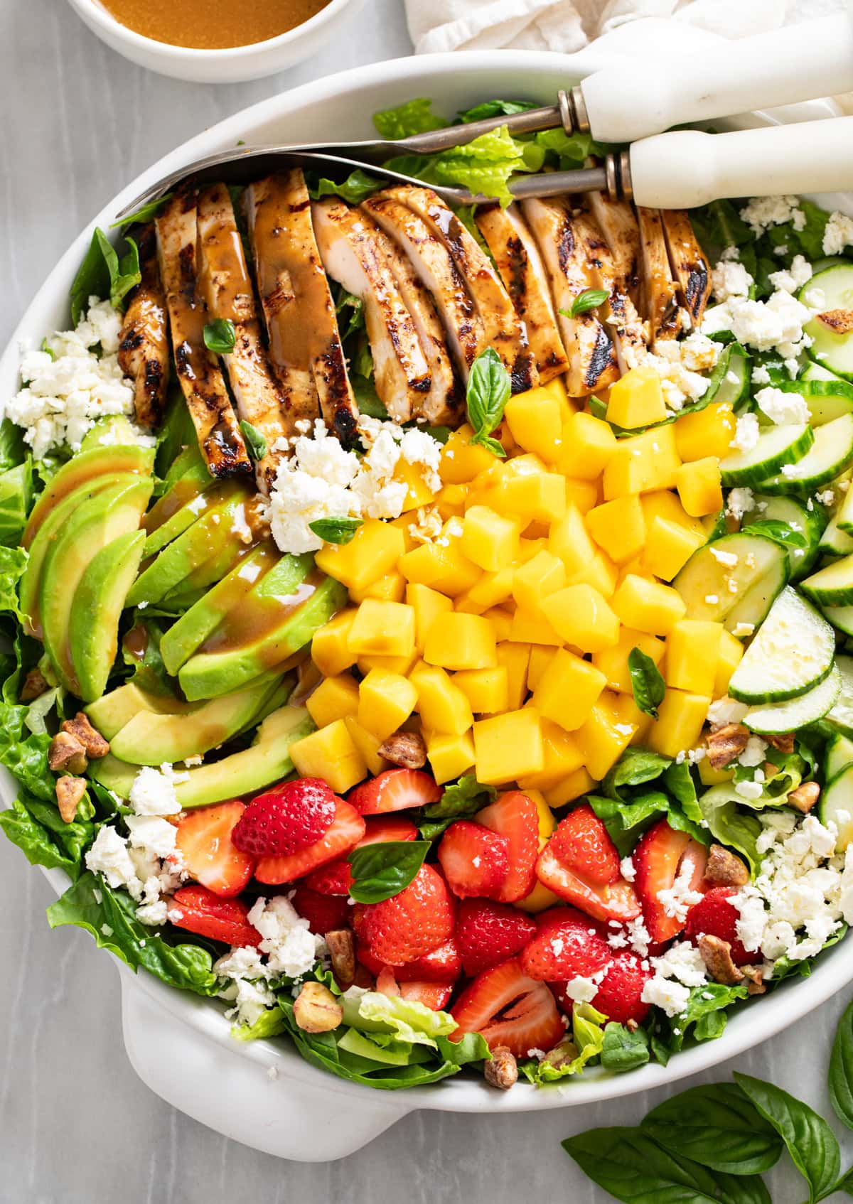 Mango Salad in a white bowl with grilled chicken, avocado, strawberry, and cucumber with mangos, feta, and dressing.