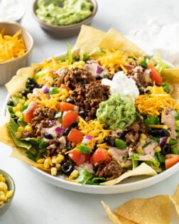 Taco Salad in a big white bowl topped with seasoned ground beef, guacamole, sour cream, and tortilla chips.