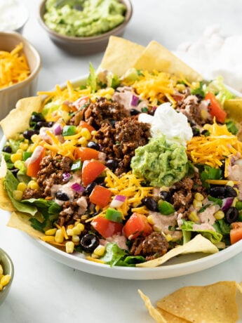 Taco Salad in a big white bowl topped with seasoned ground beef, guacamole, sour cream, and tortilla chips.
