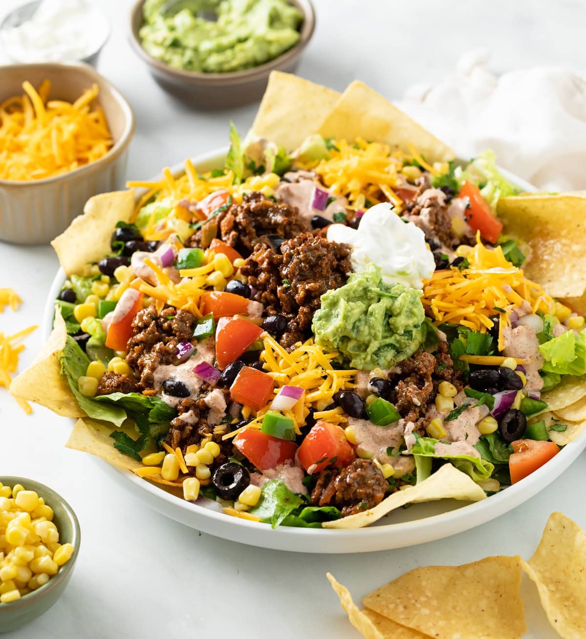 Taco Salad in a big white bowl topped with seasoned ground beef, guacamole, sour cream, and tortilla chips.