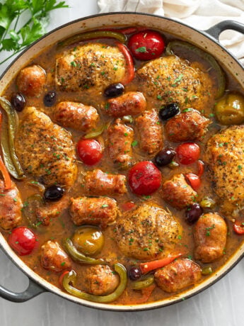 Chicken Scarpariello in a braiser with pan sauce, sausage, chicken thighs, peppers, and cherry peppers.