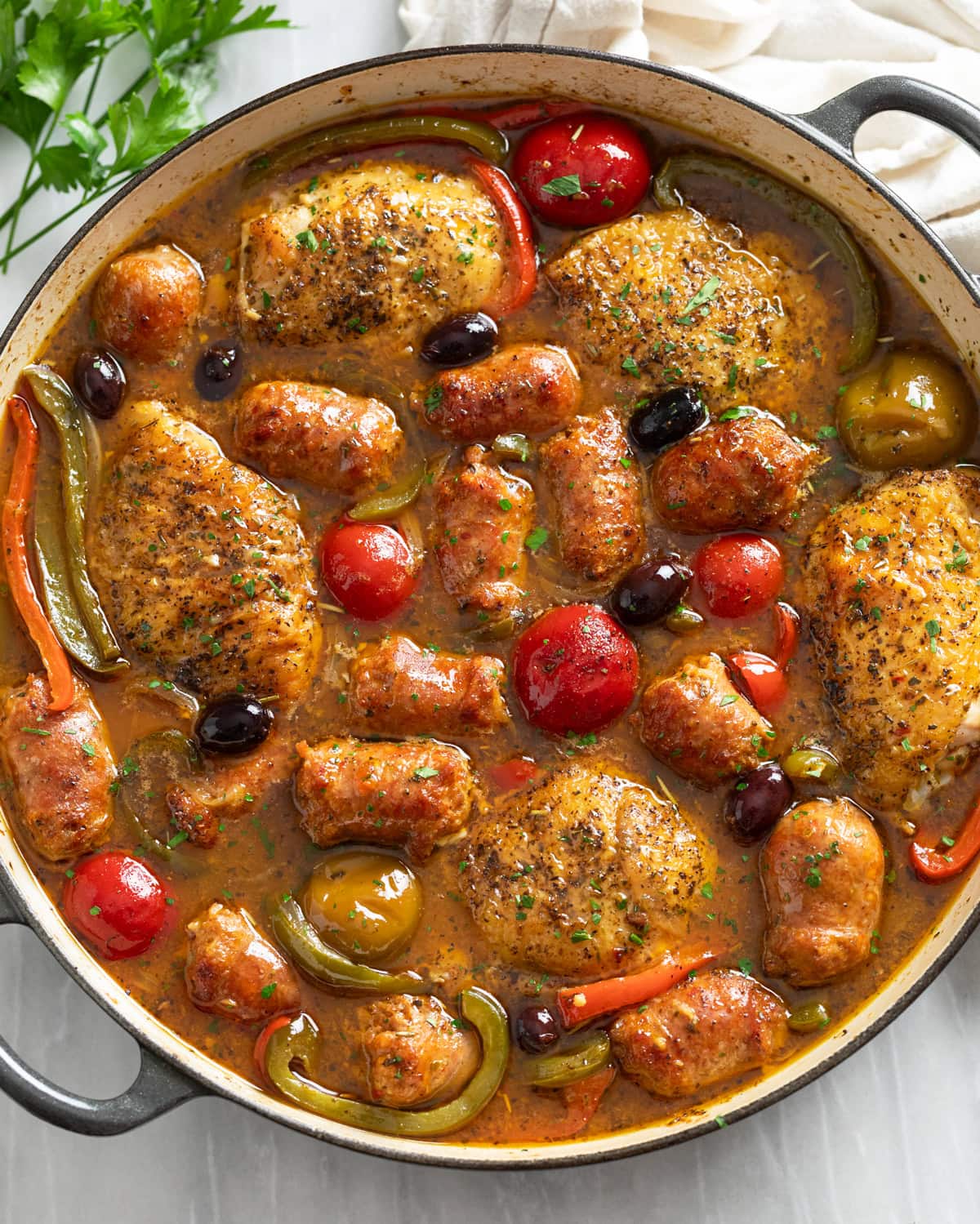 Chicken Scarpariello in a braiser with pan sauce, sausage, chicken thighs, peppers, and cherry peppers.