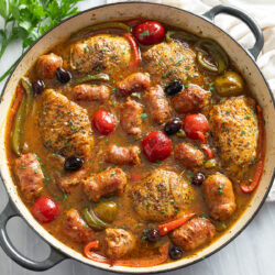 Chicken Scarpariello in a skillet with pan sauce, sausage, chicken thighs, peppers, and cherry peppers.